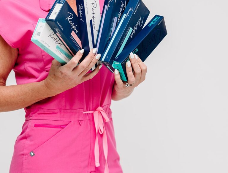 Injector in pink scrubs holding a fan of Restylane dermal filler boxes