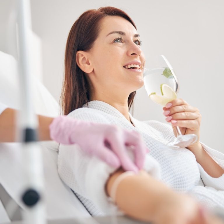 Joyous female patient drinking a healthy beverage during a medical procedure in a beauty clinic